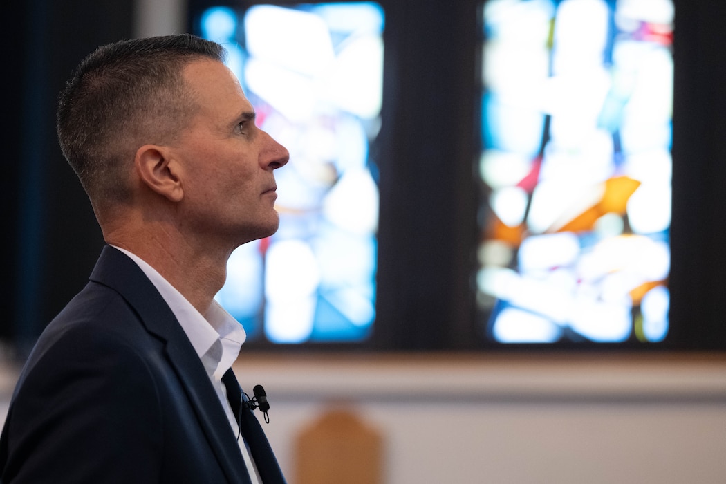 Profile of a man in a suit in front of a stained glass window.