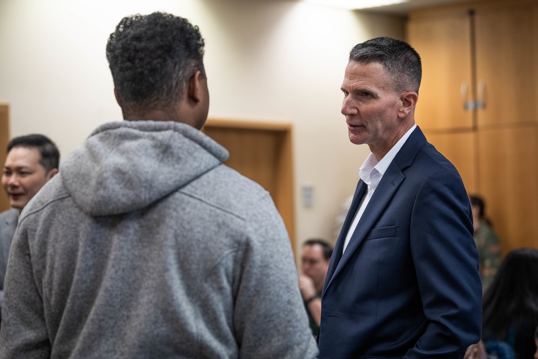 A man in a blue suit speaks with another man.