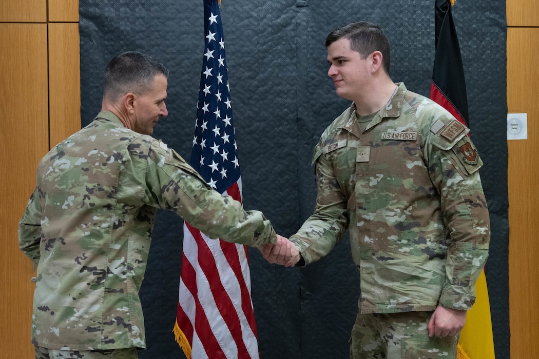 A U.S. Air Force Major General shakes hands with an Airman in front of the U.S. and German flags.