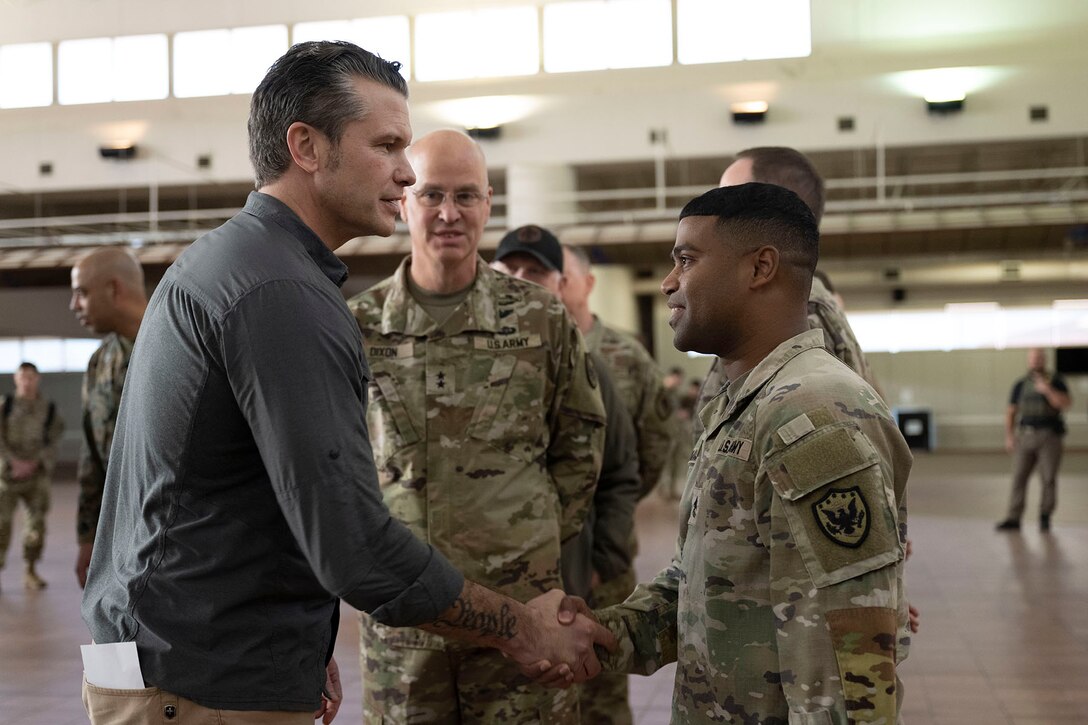 A senior defense official shakes hands with a soldier while among a group of soldiers indoors.