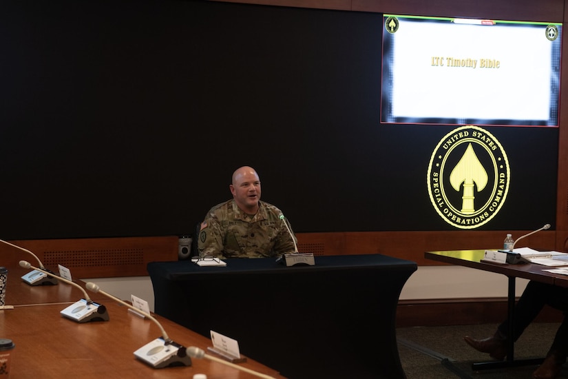 A soldier sits and speaks at a conference table.