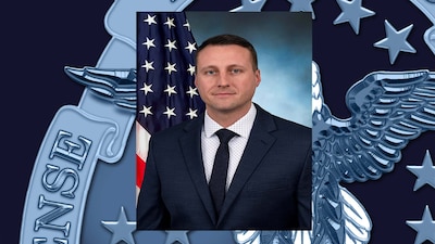 Photo of a white male in front of the America flag. He is wearing a suite.