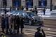 A hearse is driving down the street while uniformed service members line the street and some are saluting.