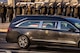 A hearse with the presidential seal on the door and a flag-draped coffin inside is driving past Navy cadets in dark overcoats and white hats who are saluting.