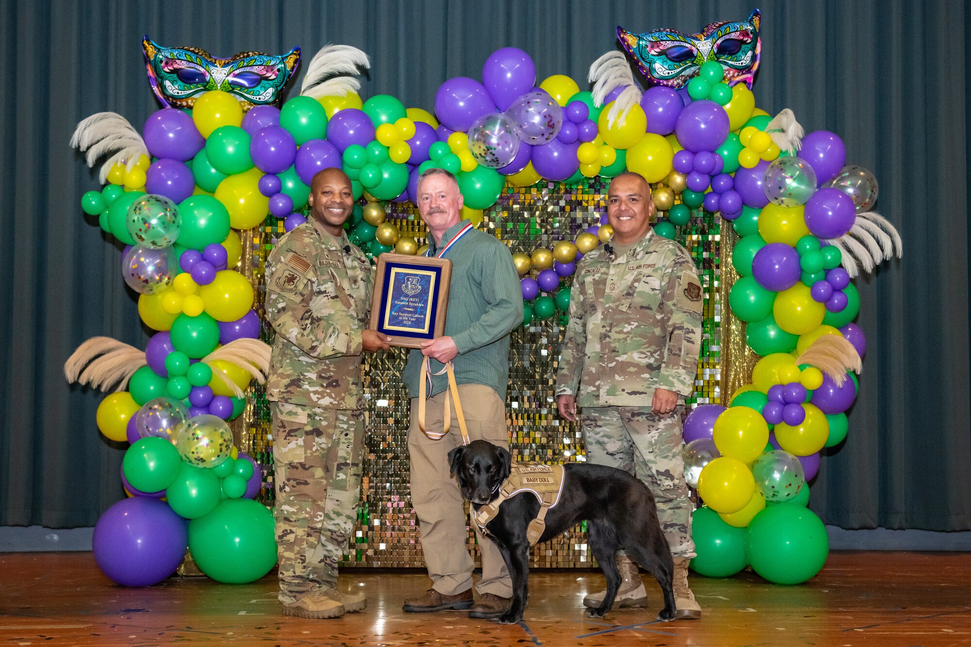 Two military members stand on either side of a civilian gentleman with his service dog. The civilian is presented a plaque award.