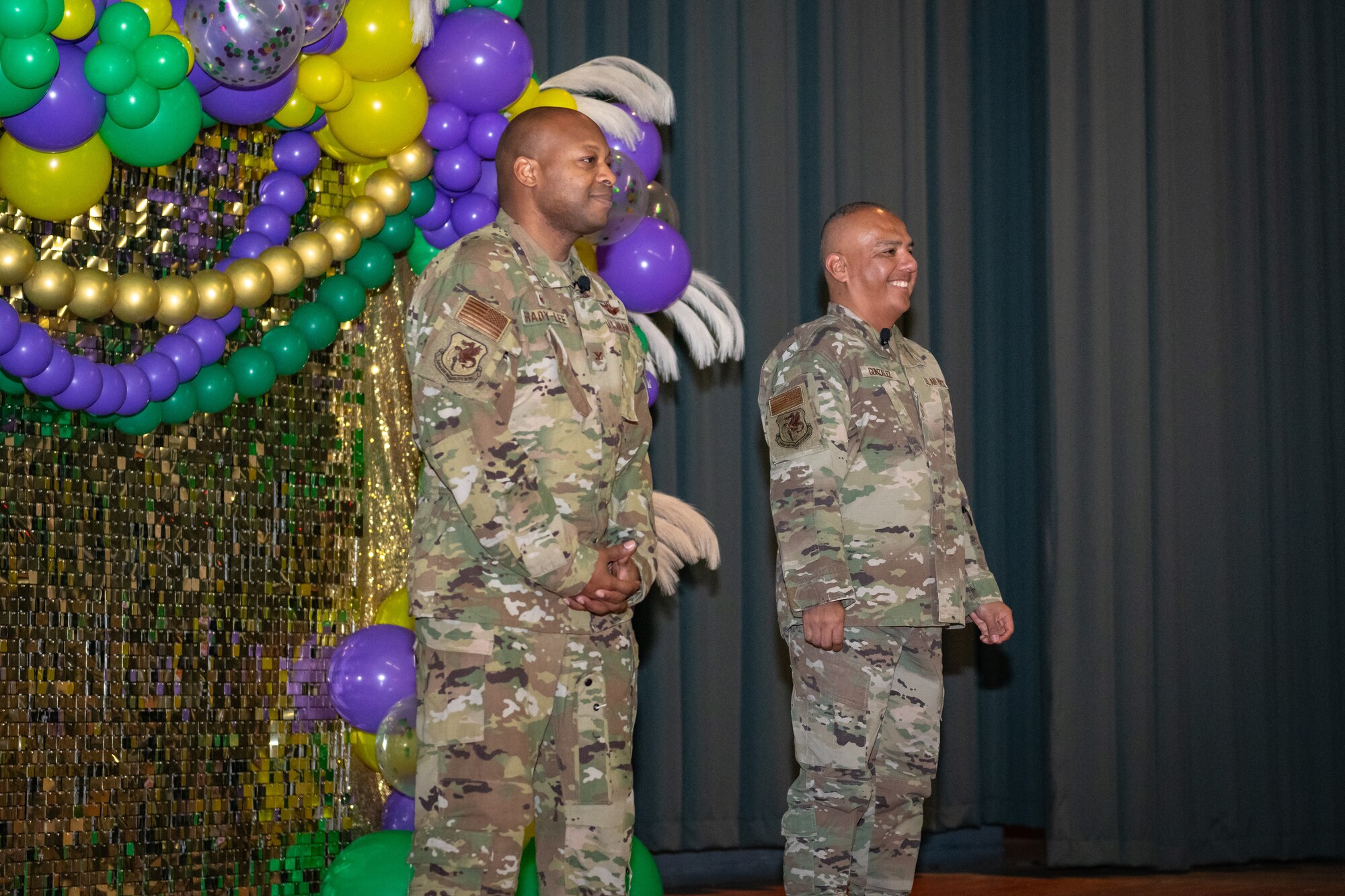 Two military members stand up on stage in front of a decorative backdrop.