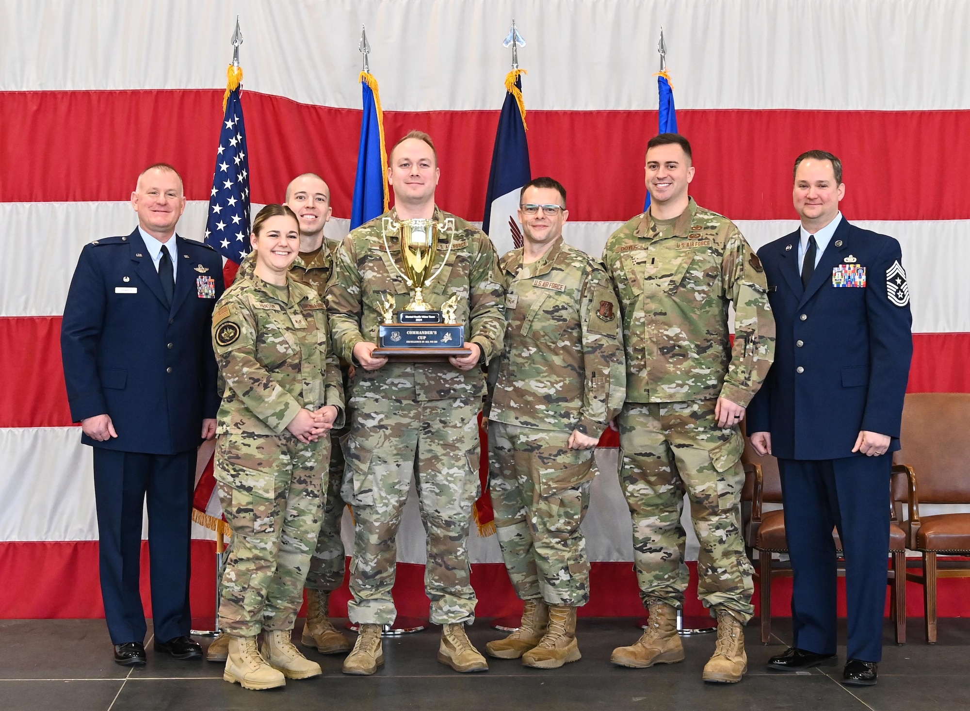 Group of Airmen pose for a photo holding a large golden trophy in front of large U.S. flag.