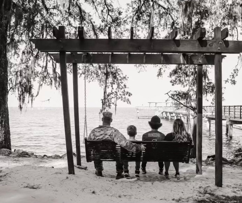 BLack and white picture of a family sitting on a bench over looking the Mobile Bay.