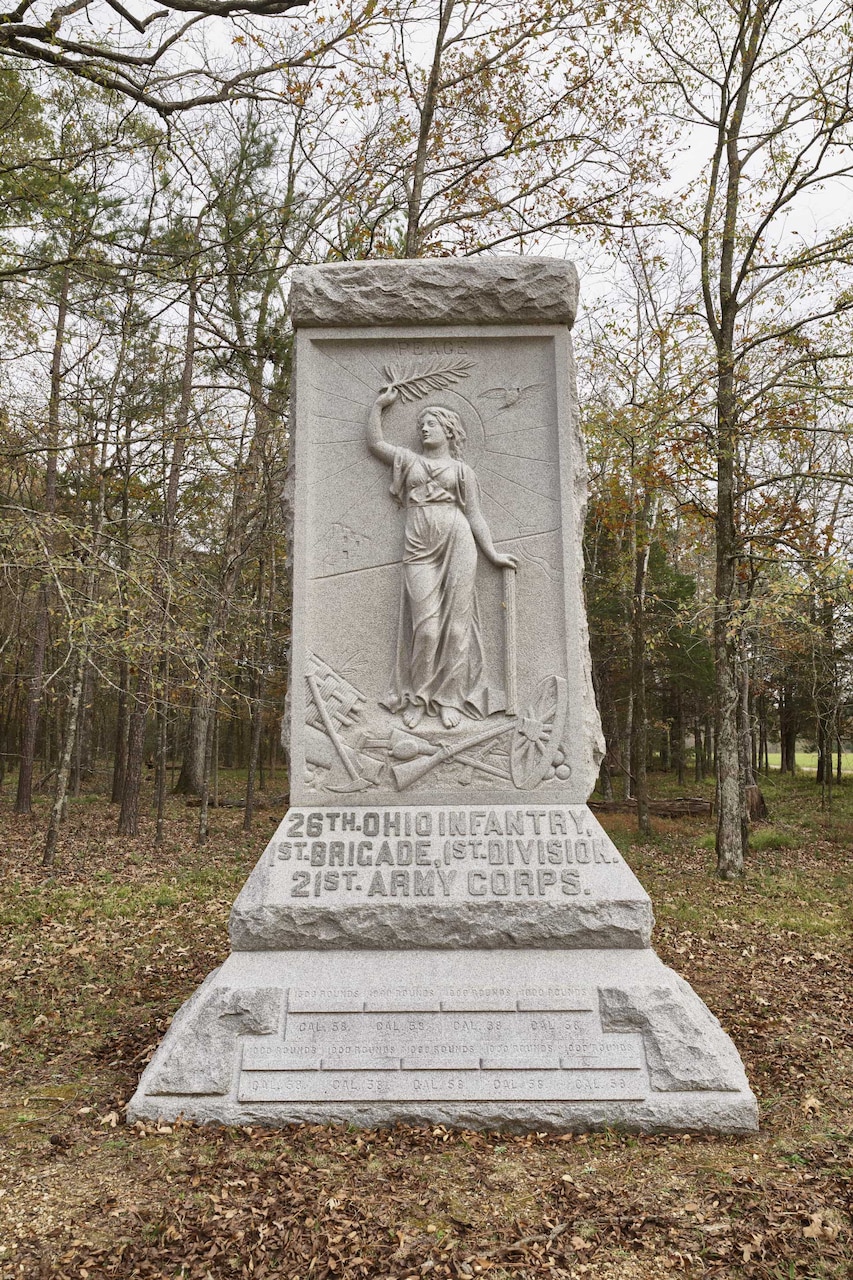 A large granite monument in a field, with forest in the background.
