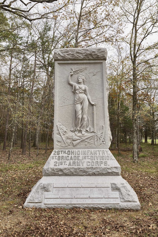 A large granite monument in a field, with forest in the background.