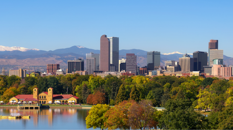Large body of water surrounded by green trees and skyscrapers with mountains in the far background
