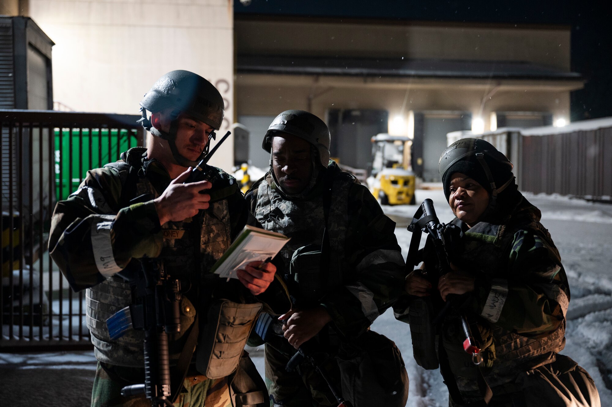 Three Airmen in protective gear use a radio to report a hazard while outside at night.