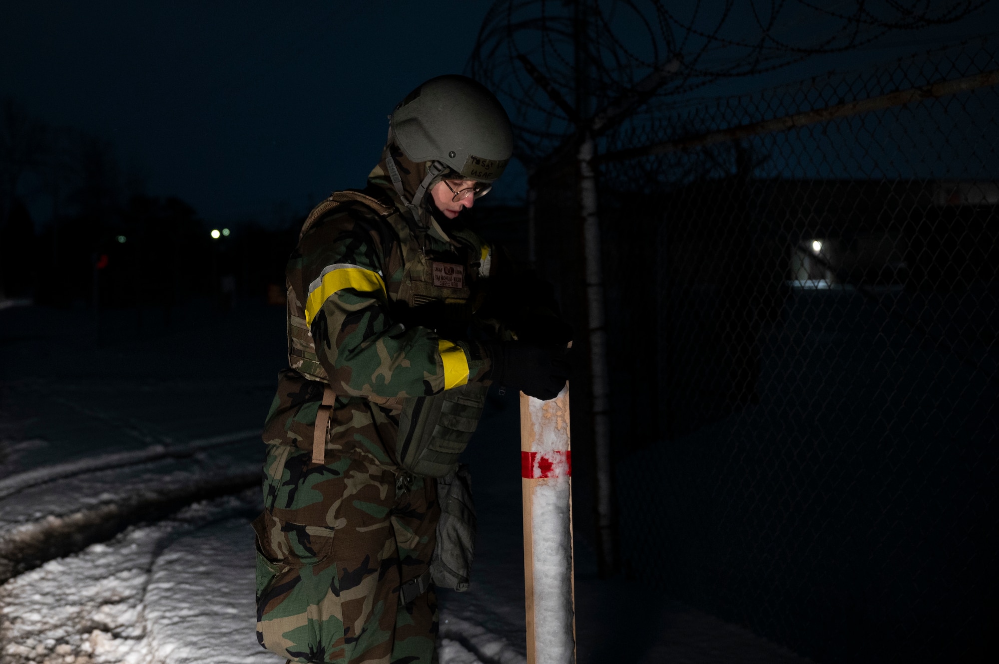 An Airman in protective gear places simulated signs of contamination while outside at night.