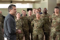 Defense Secretary Pete Hegseth stands screen left while speaking to a group of service members facing forward.