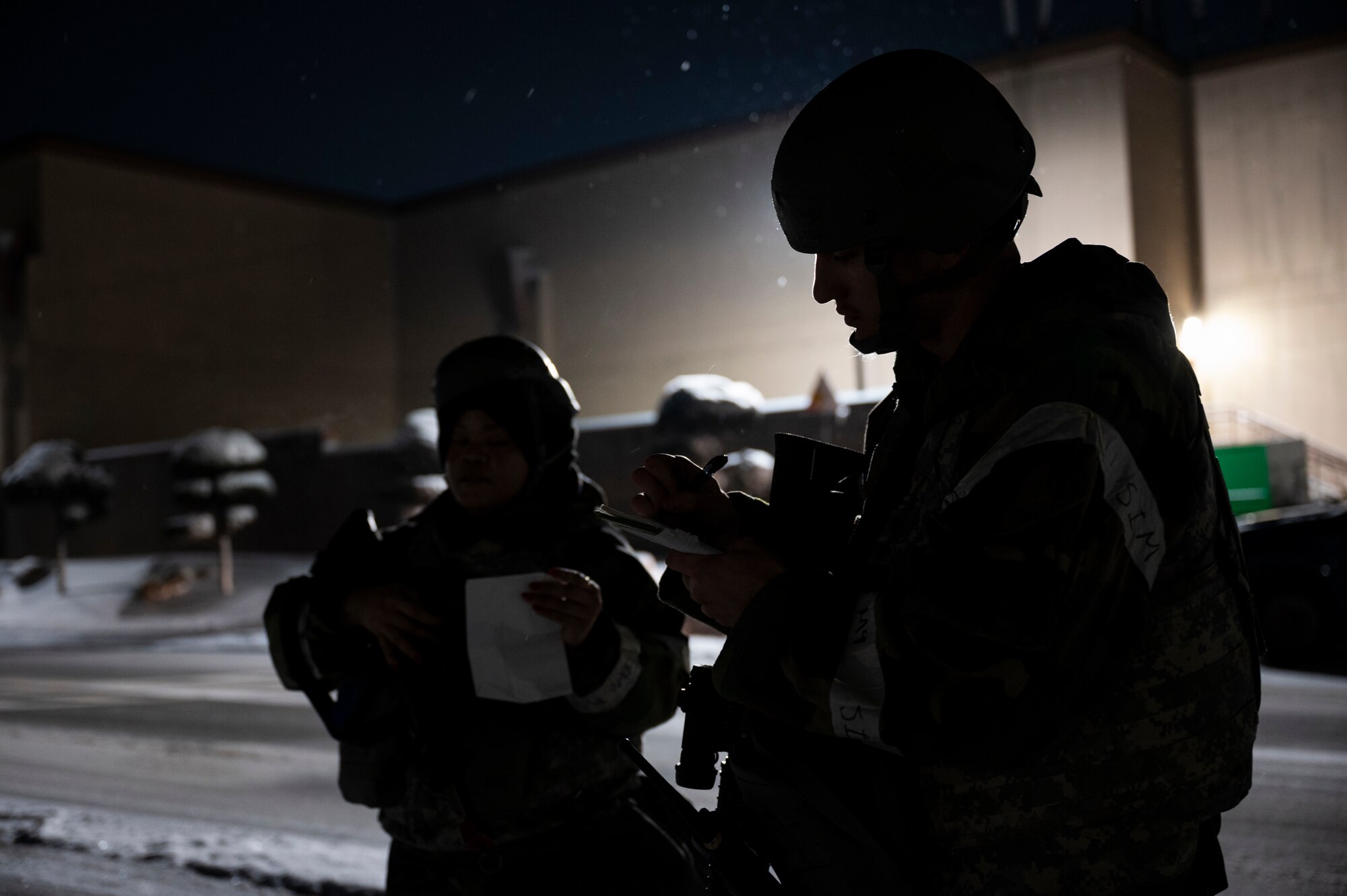 Two Airmen in protective gear make notes of a hazard while outside at night.