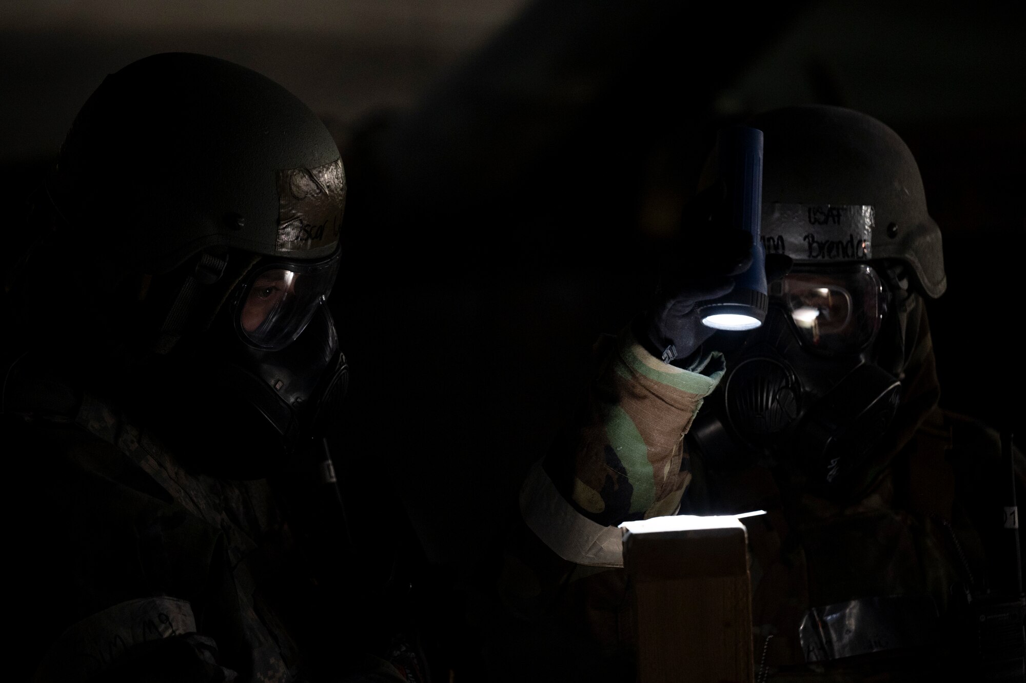 Two Airmen in protective gear look for signs of contamination while outside at night.