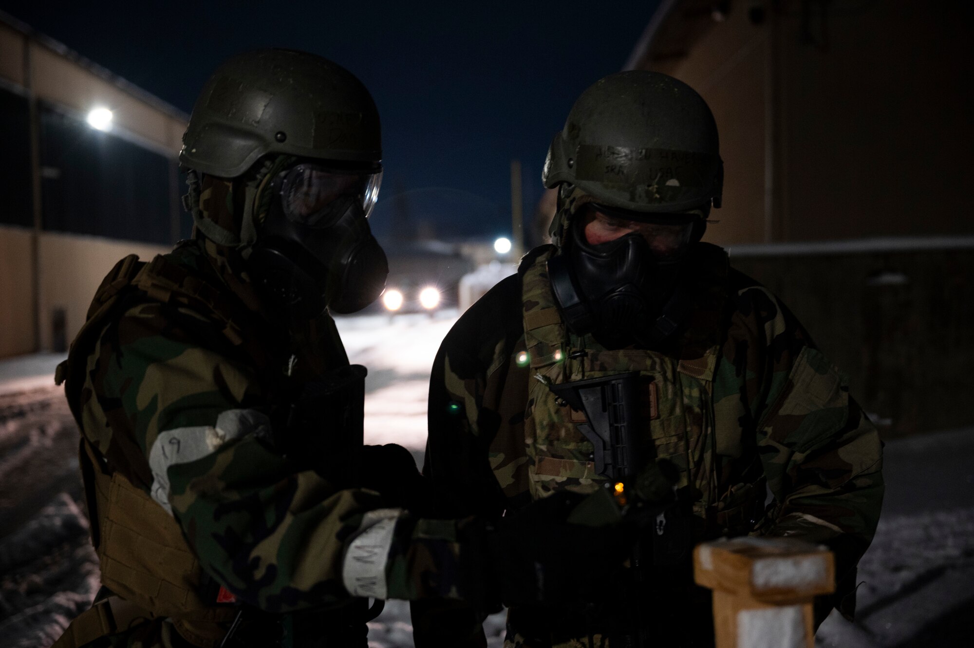 Two Airmen in protective gear look for signs of contamination while outside at night.