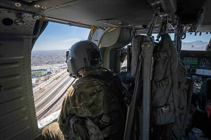 A pilot looks out of a helicopter at a highway under blue skies.