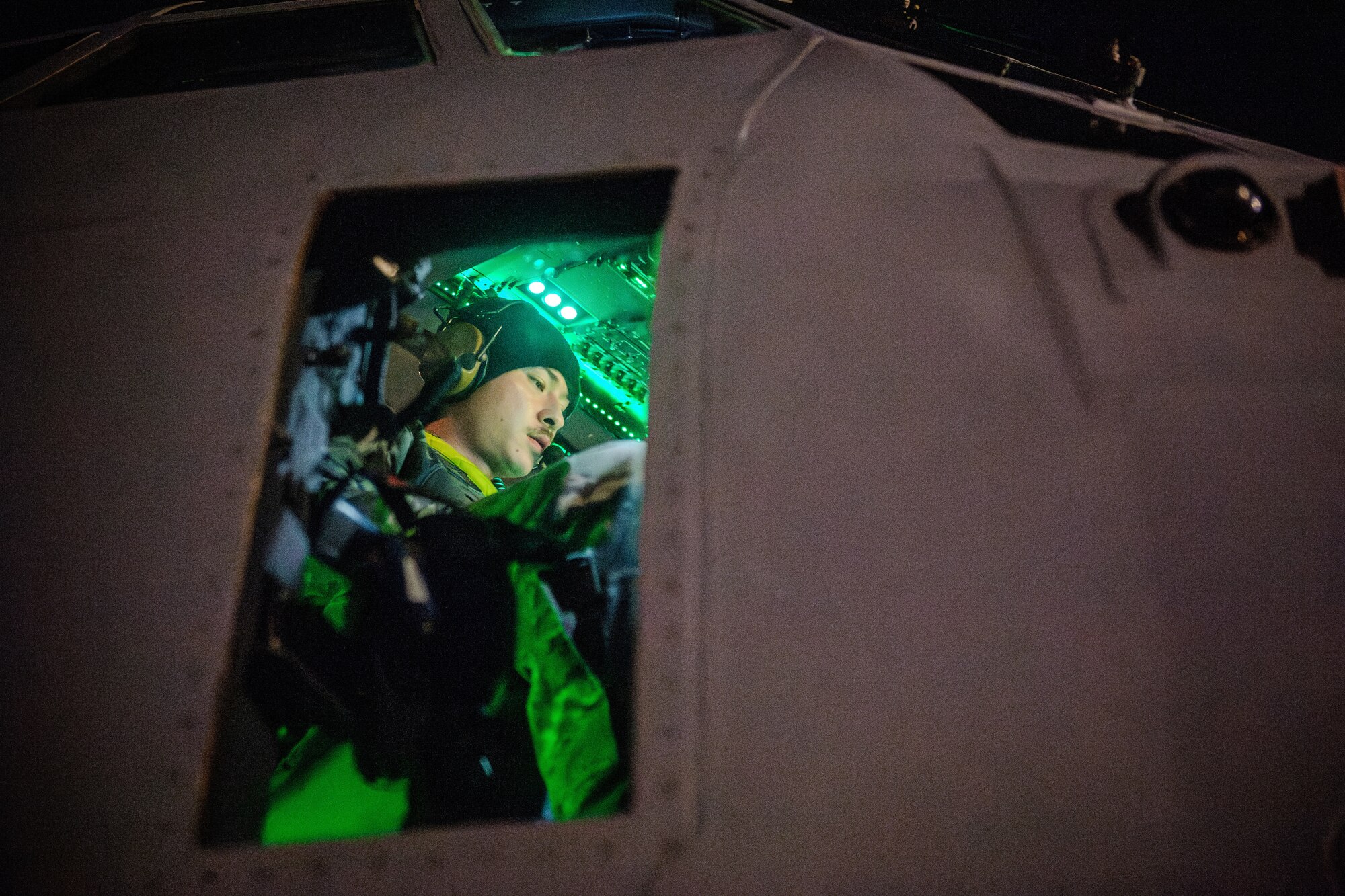 An Airman sits in a cockpit illuminated by green lighting.