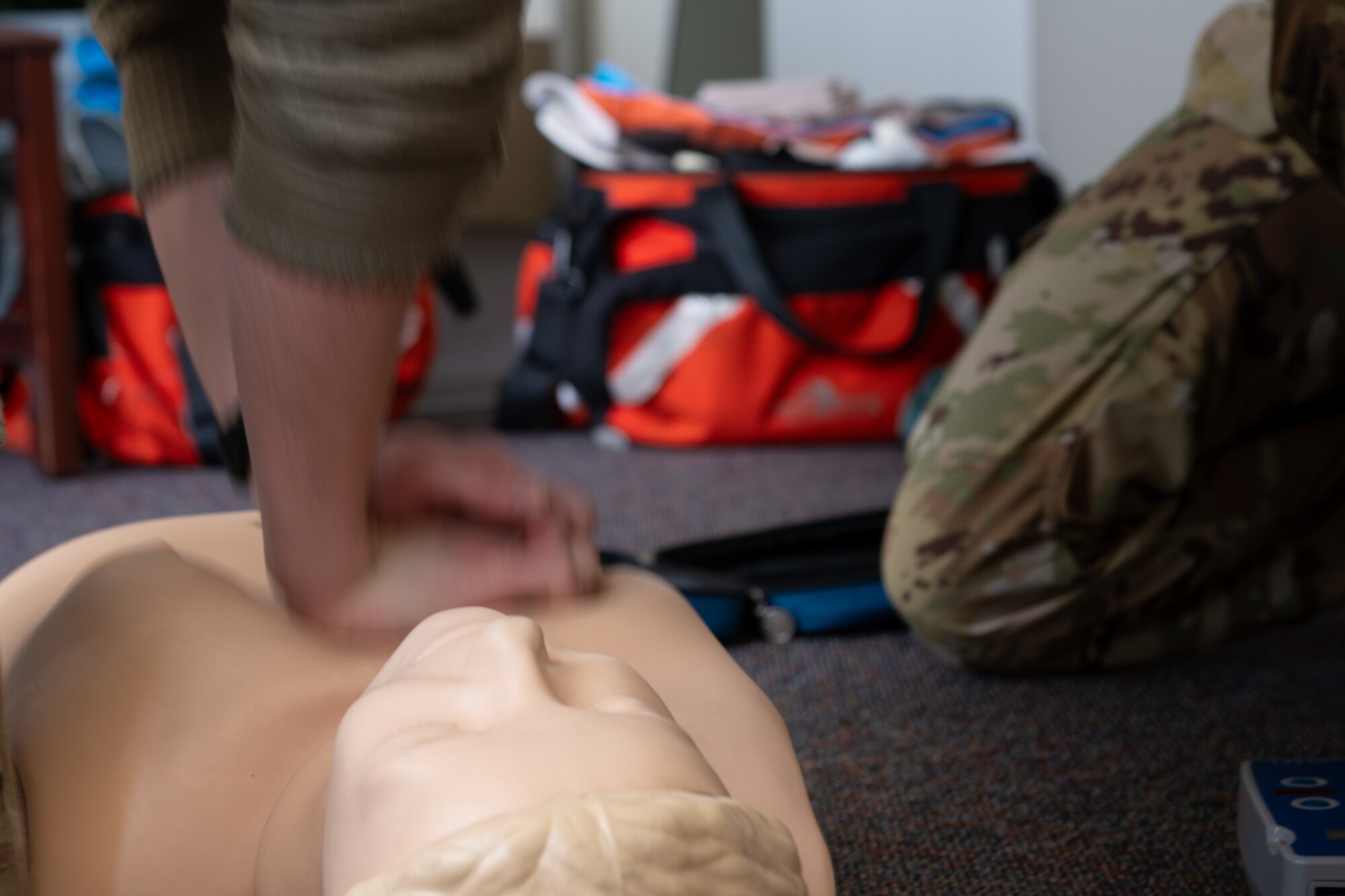 An Airman performs chest compressions on a yellow dummy.