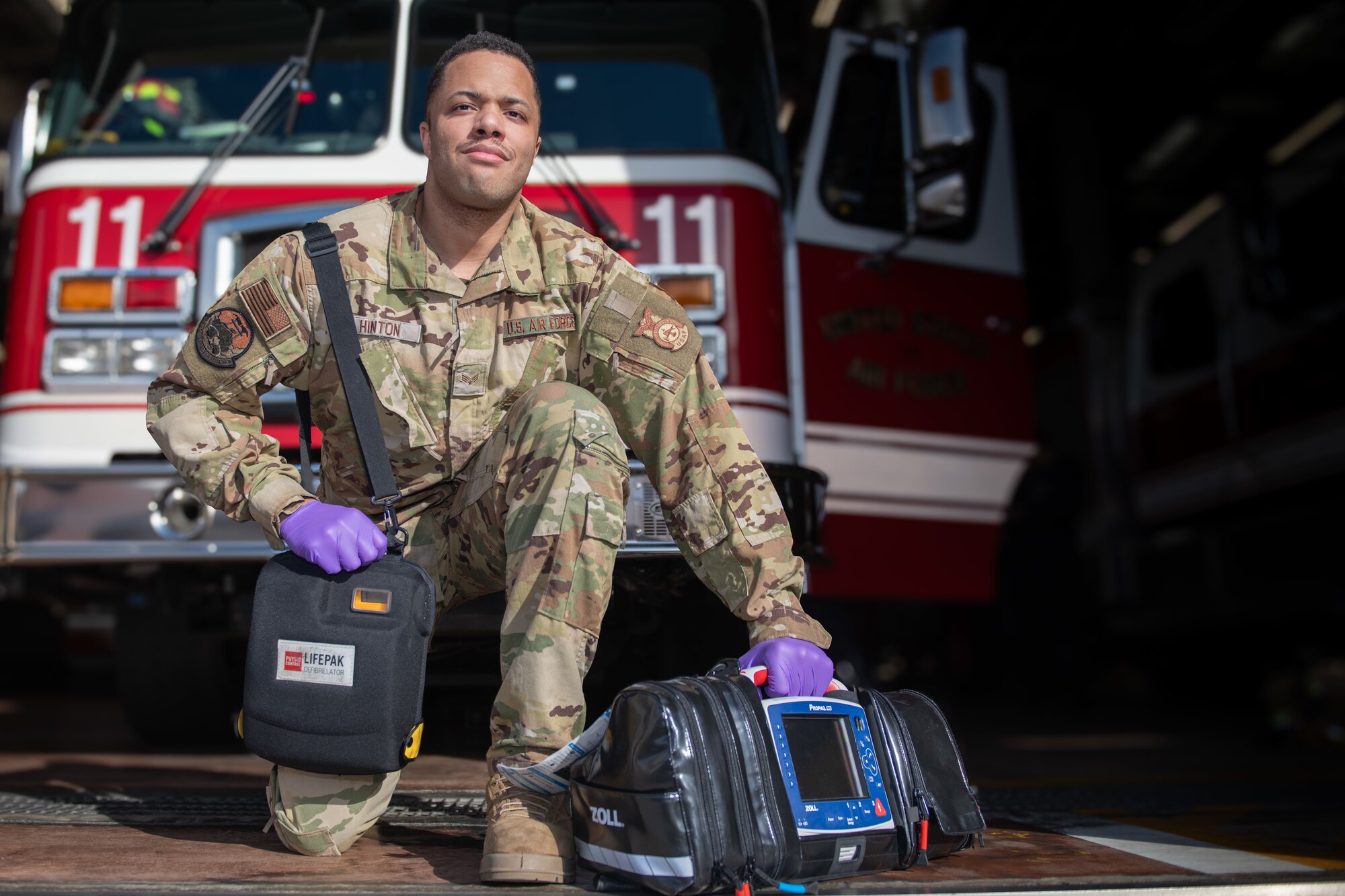 An Airman poses for a photo while holding medical equipment in front of a red fire truck.