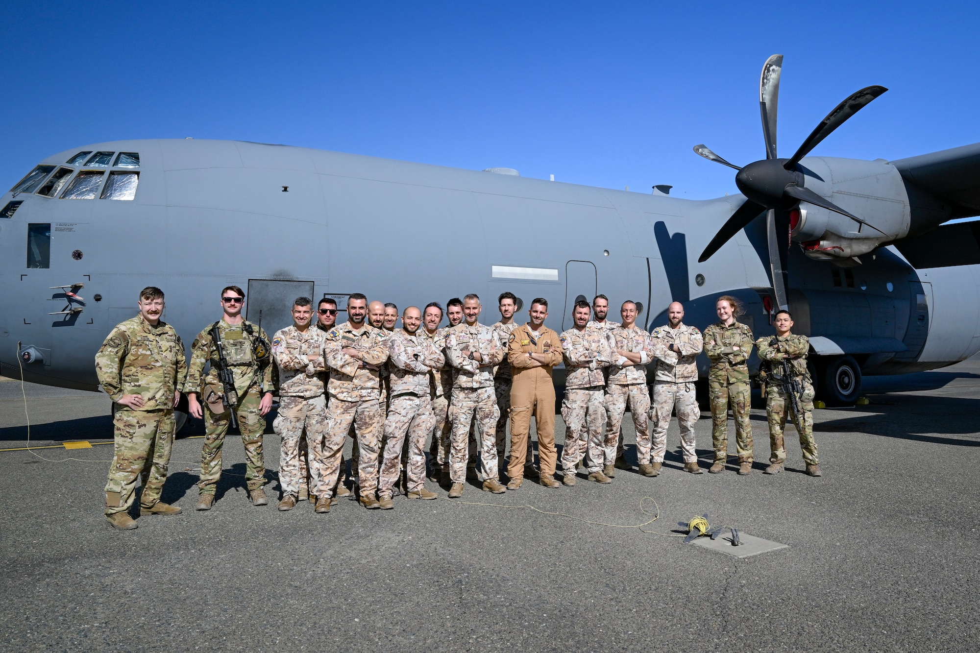 A group of U.S. Air Force and Italian Air Force personnel pose for a photo in front of a C-130J aircraft.