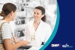 Female pharmacist wearing white lab coat stands behind pharmacy counter speaking to female patient.
