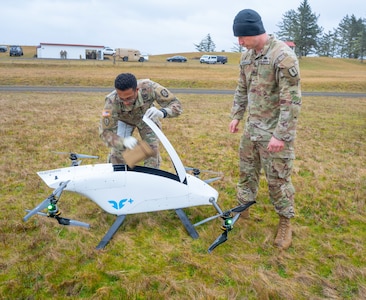 Sgt. 1st Class Kenneth Day retrieves simulated blood supplies delivered by a blueflite drone while Sgt. Benjamin Keikkala provides security during a field training exercise at Camp Rilea, Oregon, Jan. 30, 2025. The innovative drone delivery system demonstrated rapid resupply capabilities for combat medics in tactical environments.