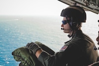 Coast Guard Petty Officer 2nd Class David Narkis, an aviation maintenance technician assigned to Coast Guard Air Station Barbers Point, sits on the aft ramp of an HC-130 Hercules airplane during a training mission