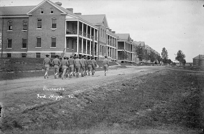 black and white image from the Library of Congress National Photo  shows a group of Soldiers marching down a dirt road, now the paved Sheridan Avenue, alongside the U.S. Army barracks Bldg. 250.