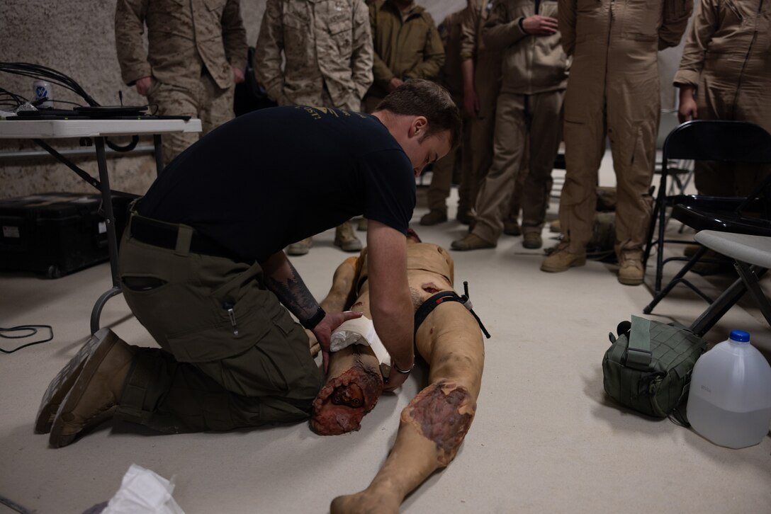 U.S. Navy Hospital Corpsman 2nd Class Joseph Simon, from Michigan, a search and rescue medical technician with 1st Medical Battalion, 1st Marine Logistics Group, wraps a gauze around the leg of an imitation casualty to demonstrate proper Tactical Combat Casualty Care (TCCC) techniques to Marines with Marine Light Attack Helicopter Squadron (HMLA) 269 during a level II TCCC skills class at Marine Corps Air Ground Combat Center Twentynine Palms, California, Jan. 28, 2025. HMLA-269 and other squadrons assigned to 2nd Marine Aircraft Wing trained to integrate with and support Marine ground units during Service Level Training Event (SLTE) 1-25, a series of training events designed to prepare Marines for operations around the globe. (U.S. Marine Corps photo by Cpl. Anakin Smith)