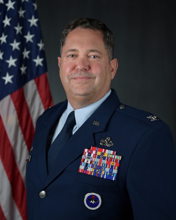 Air Force member in uniform in front of the U.S. flag.