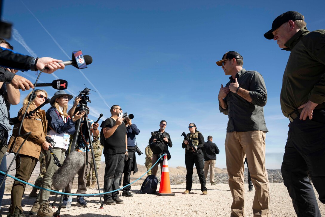 Senior defense civilians speak to members of the press outside in an arid field.