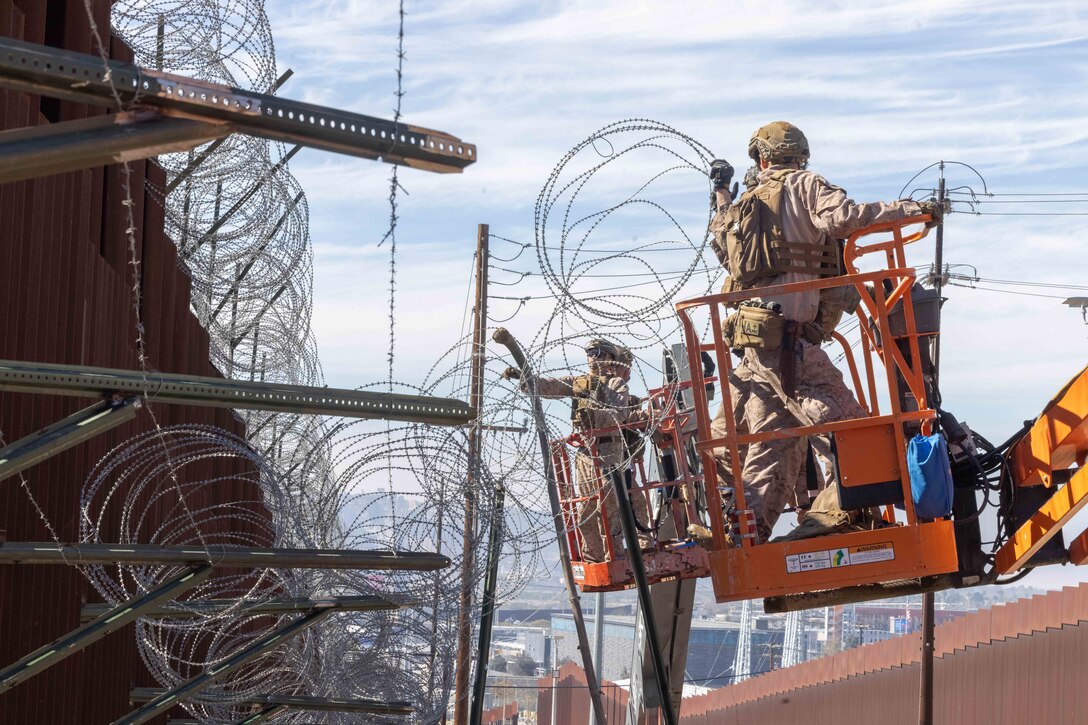 Marines use a lift to place concertina wire along a wall during the day.
