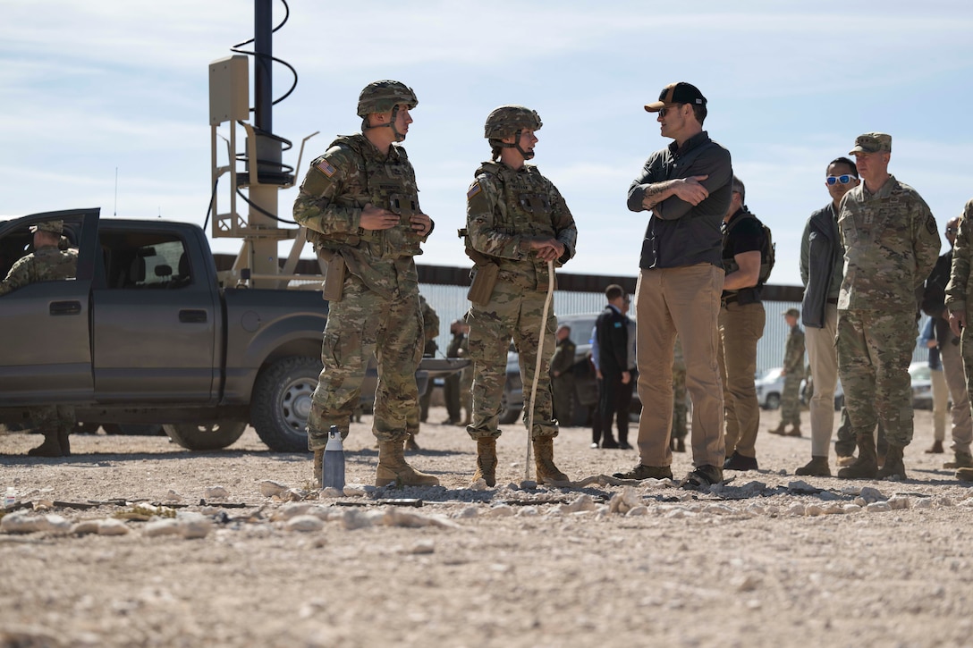 A senior government official speaks with soldiers outside on arid terrain during the day.