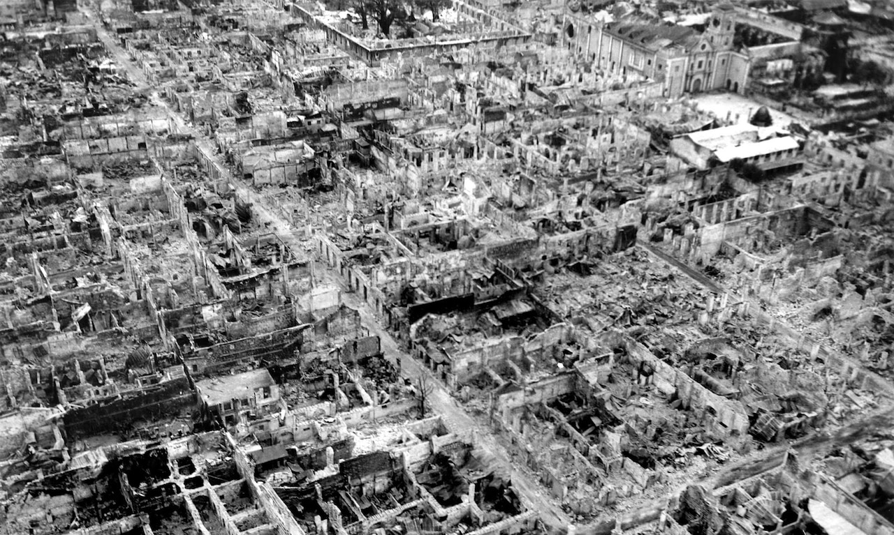 An aerial view of a war-torn city is shown.