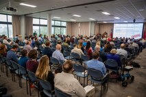 Person delivers presentation in front of a large group of seated people