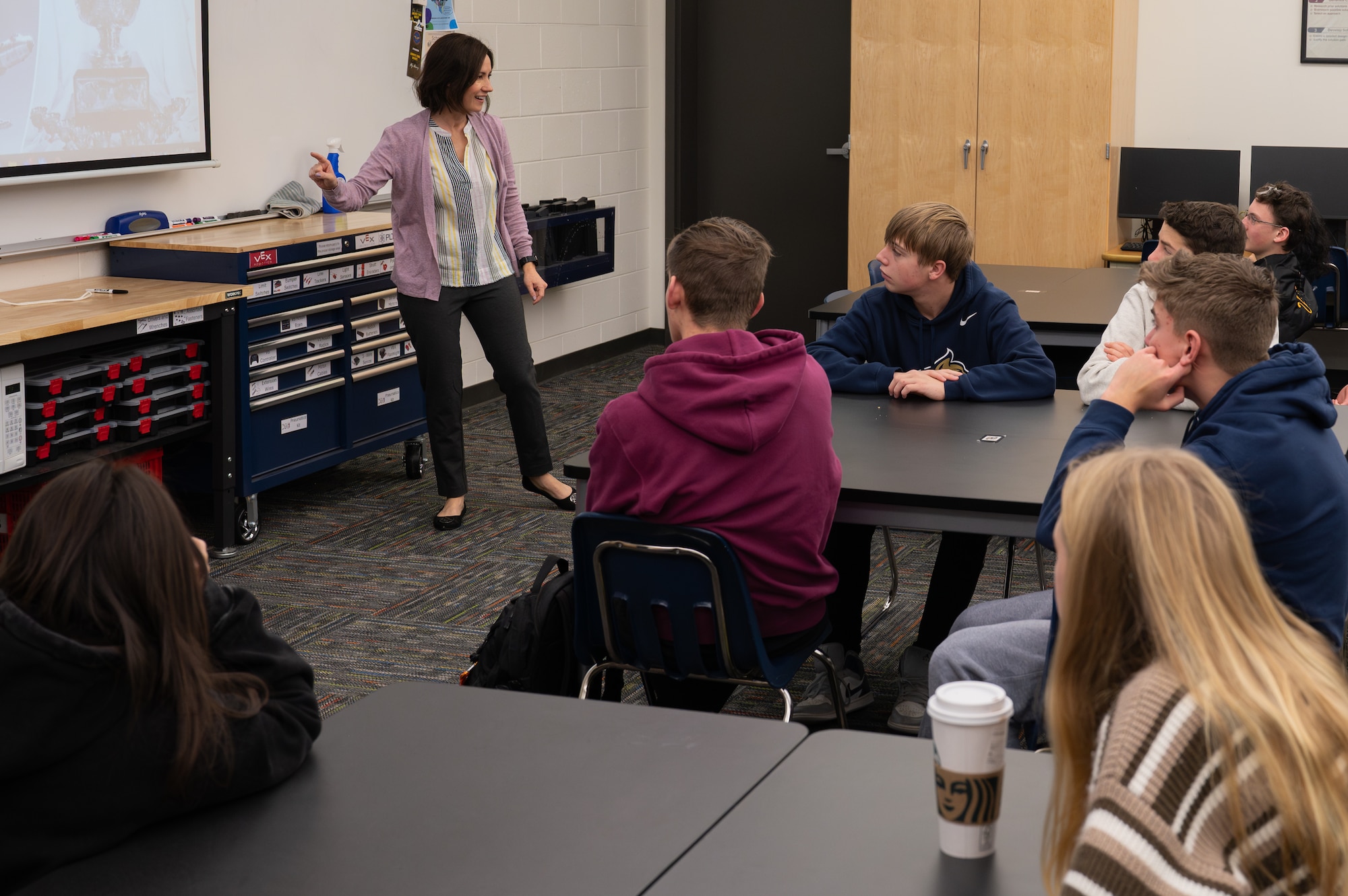 An individual standing in front of a high school class giving a presentatoin.