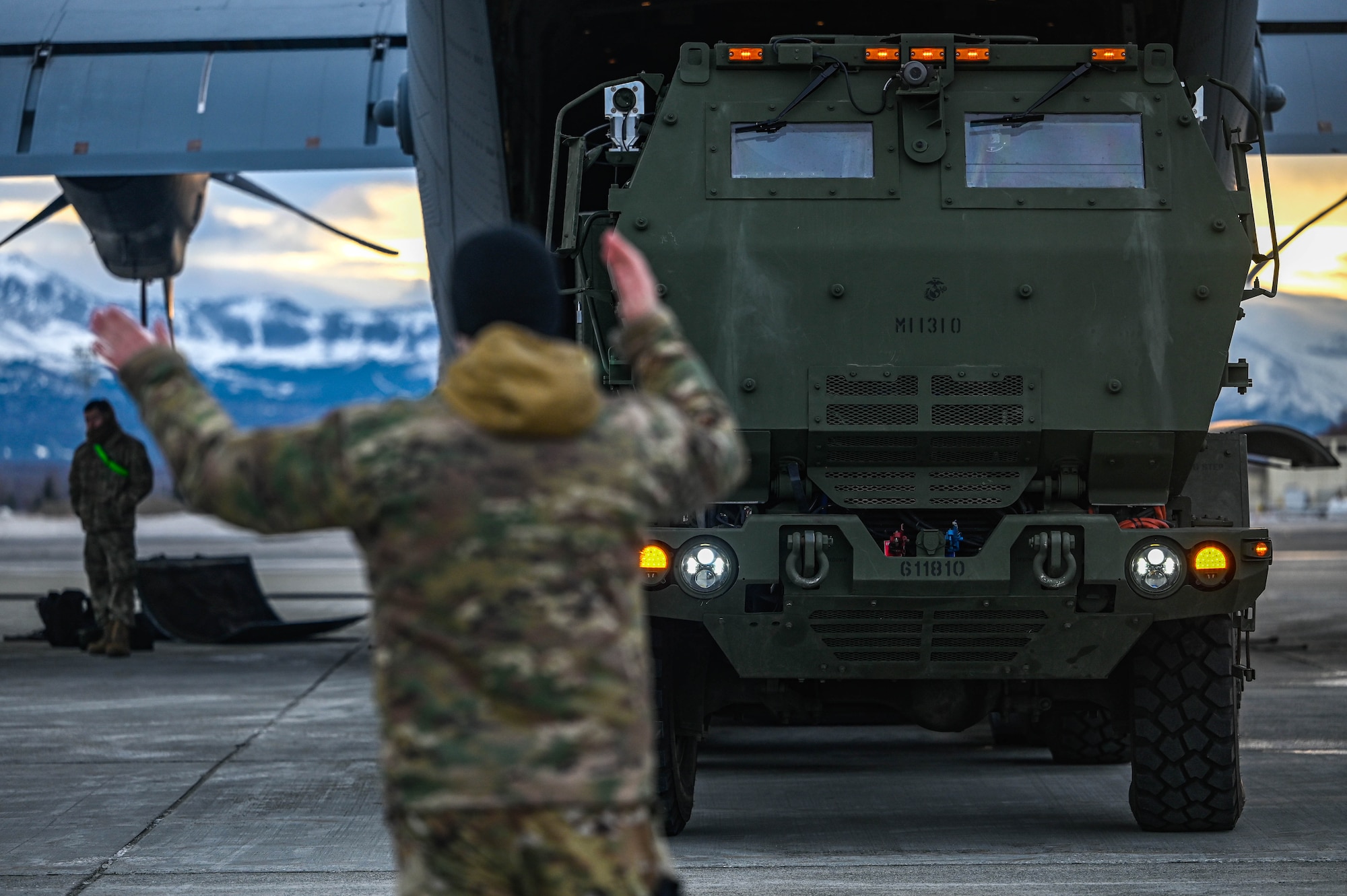 A loadmaster, assigned to the 61st Airlift Squadron, marshals a High Mobility Artillery Rocket System (HIMARS), assigned to the 1st Battalion, 11th Field Artillery Regiment,  into the back of a C-130J Super Hercules aircraft during the Joint Pacific Multinational Readiness Center (JPMRC) 25-02 exercise at Joint Base Elmendorf-Richardson, Alaska, Jan. 18, 2025. Conducting HIMARS training showcases the 19th Airlift Wing crew’s combat readiness and quick-precision-striking ability by rapidly onloading, offloading and mobilizing the HIMARS.