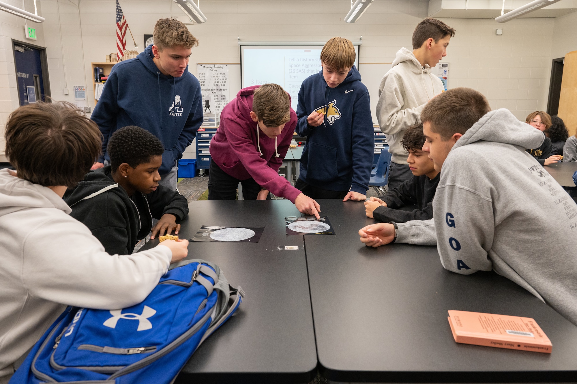 A group of students leaning over a table to look at a photo.