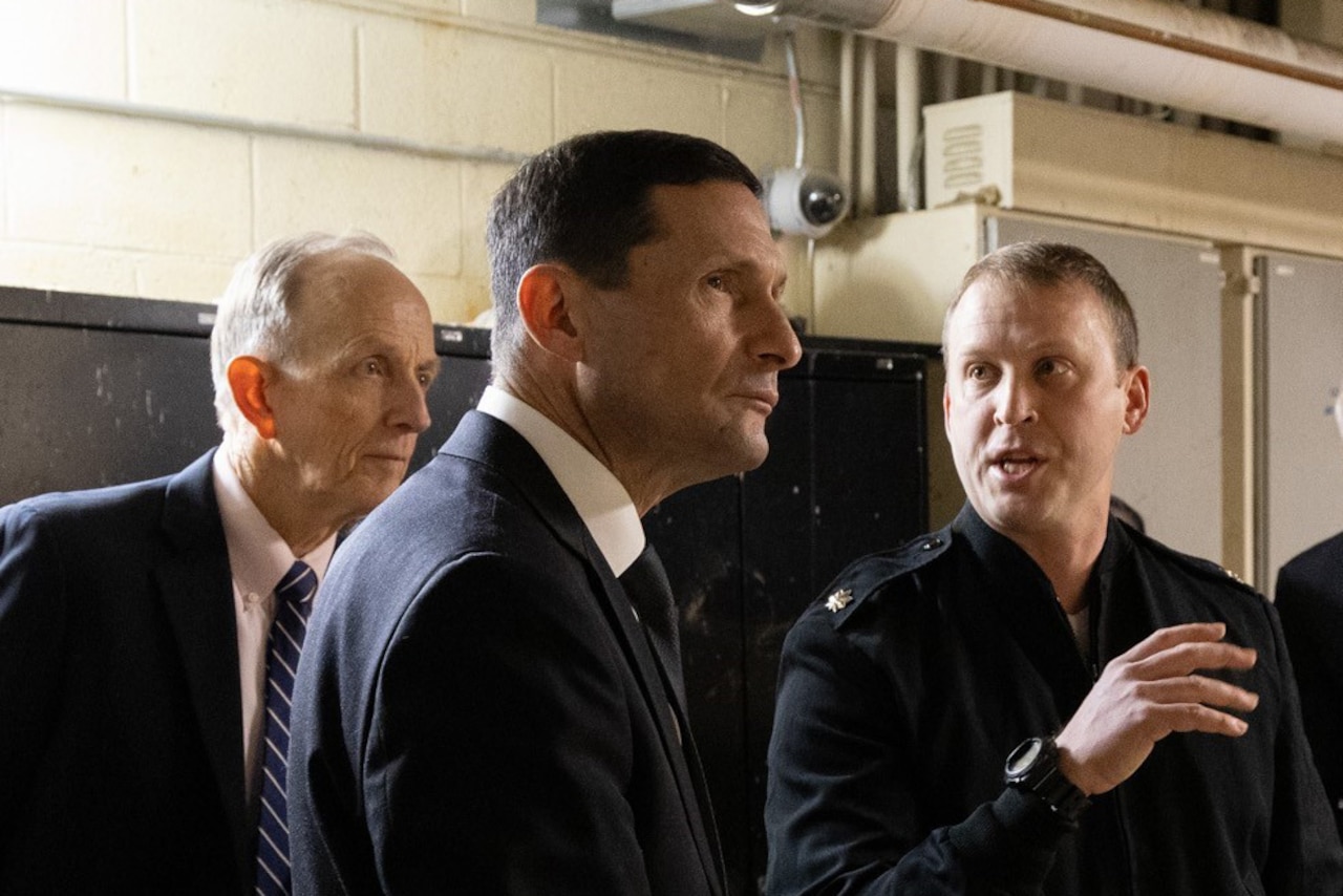 Three men wearing suits standing in a room with pipes.