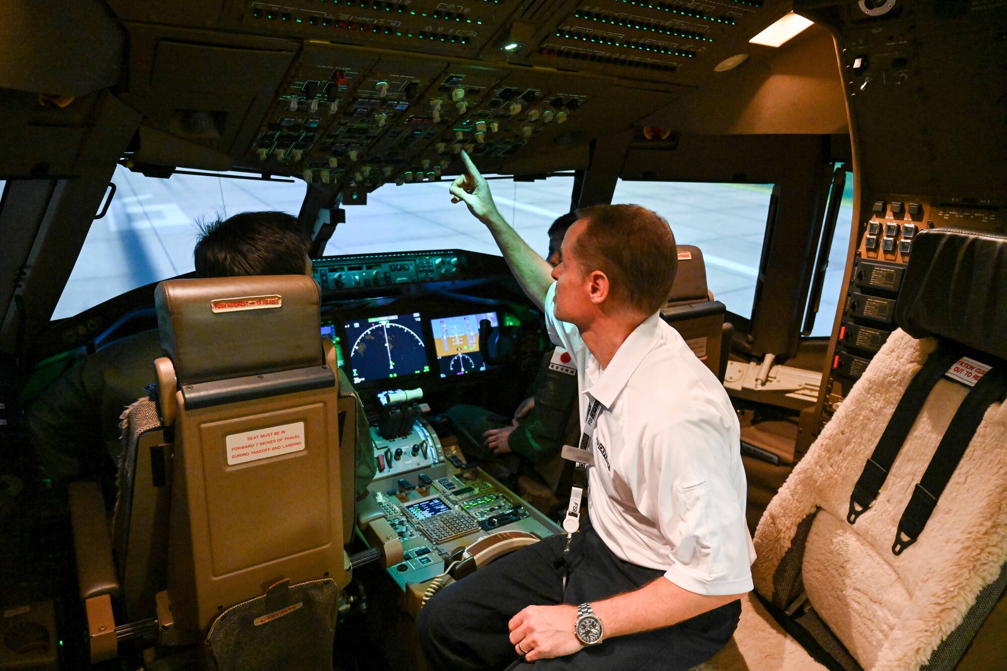 Nicola Borghini, Flight Safety International KC-46 Pegasus aircraft lead pilot instructor, points out aspects of a KC-46 simulator to Japanese Air Self-Defense Force Maj. Yohei Uramoto and Maj. Yoshiaki Fujii, 405th Air Refueling Squadron KC-46 pilots, at Altus Air Force Base, Oklahoma, Nov. 6, 2024. Yohei and Fujii shared that the most challenging part of their training was mastering the English language. (U.S. Air Force photo by Airman 1st Class Lauren Torres)(This photo has been altered for security purposes by blurring out identification badges)