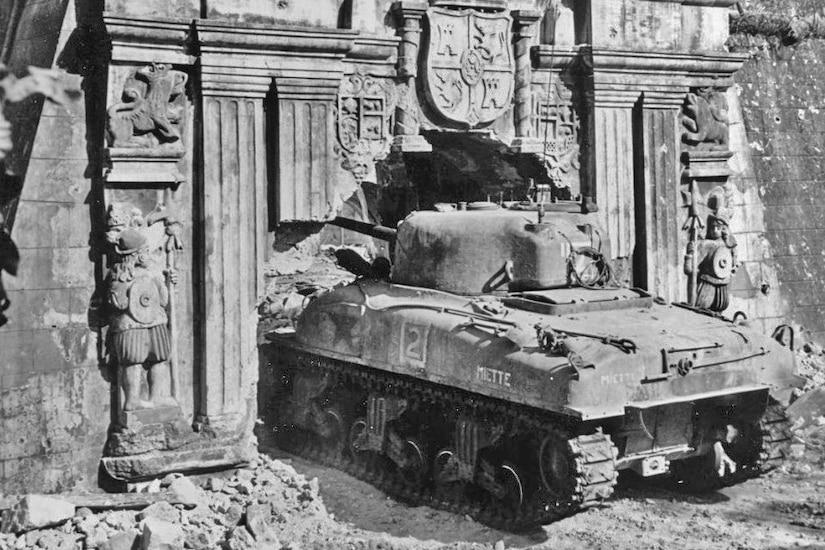 A tank sits amongst the rubble of a war-torn building.