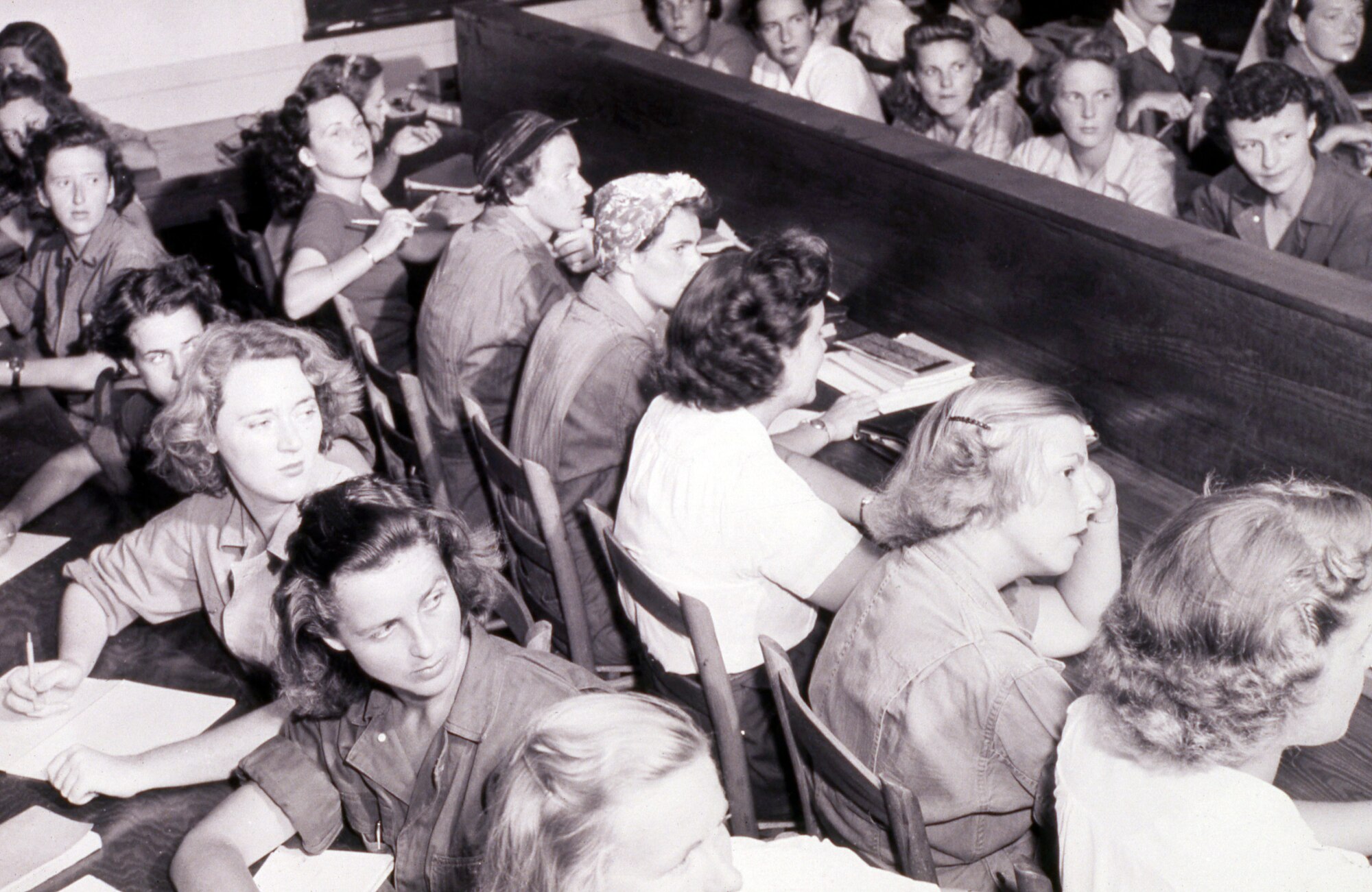 WASP Trainees sitting at desks with books, paper and pencils, listening to an instructor that is not pictured.