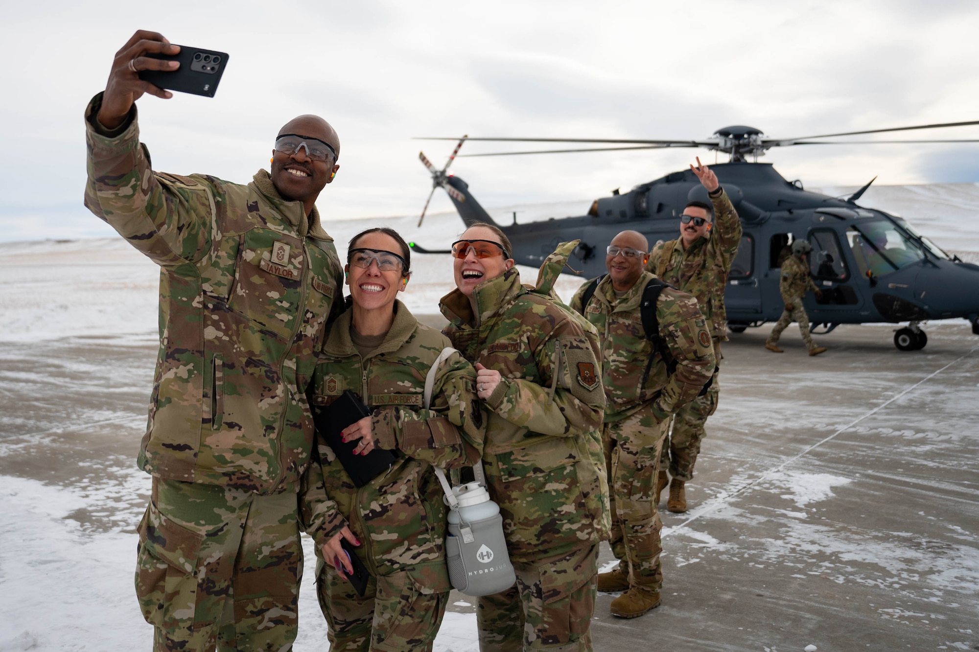 A group of uniformed personnel take a selfie in front of a helicopter.