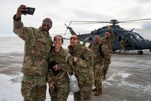 A group of uniformed personnel take a selfie in front of a helicopter.