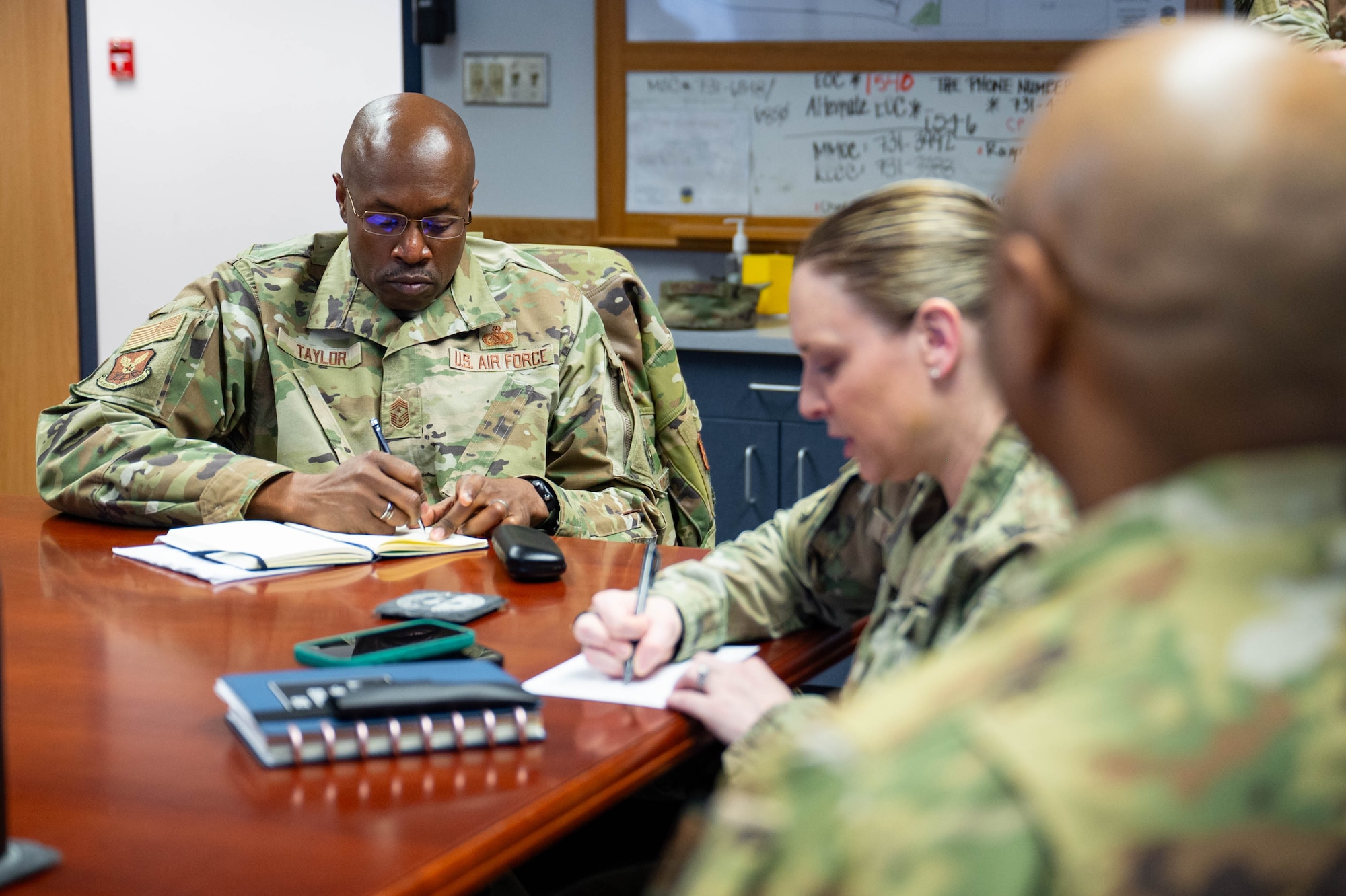 A group of uniformed personnel sit around a table taking notes.