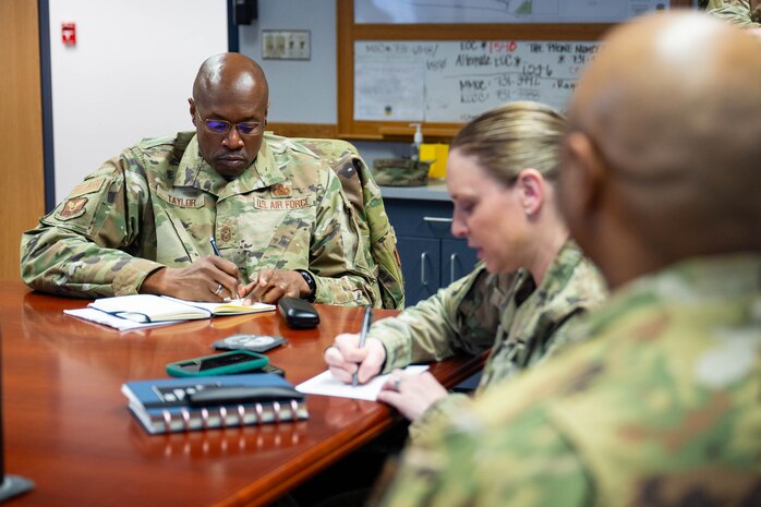 A group of uniformed personnel sit around a table taking notes.