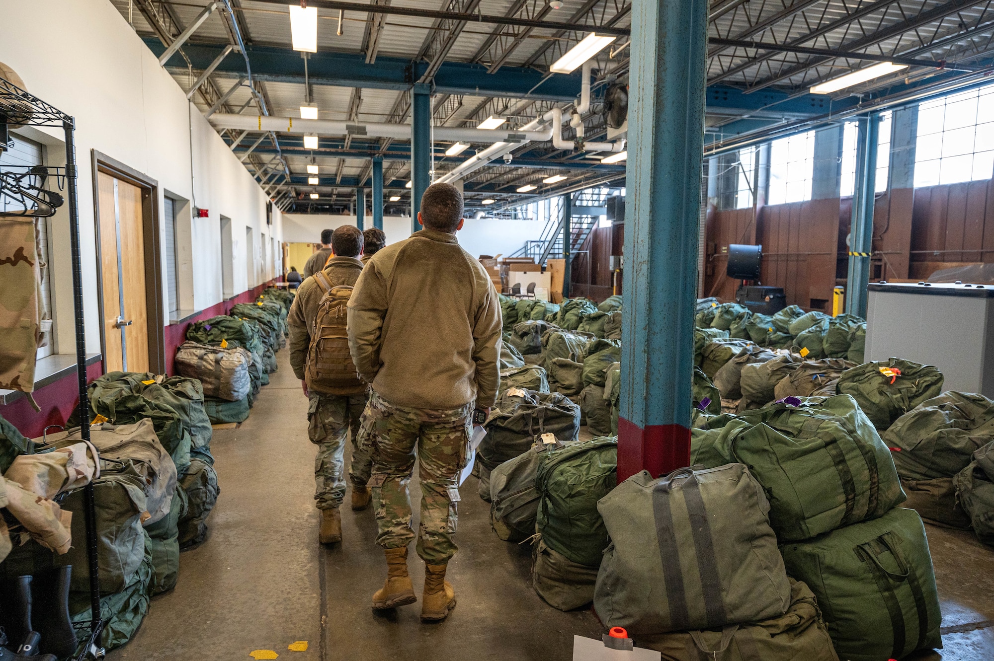 Airmen walk in a line by green bags in a warehouse