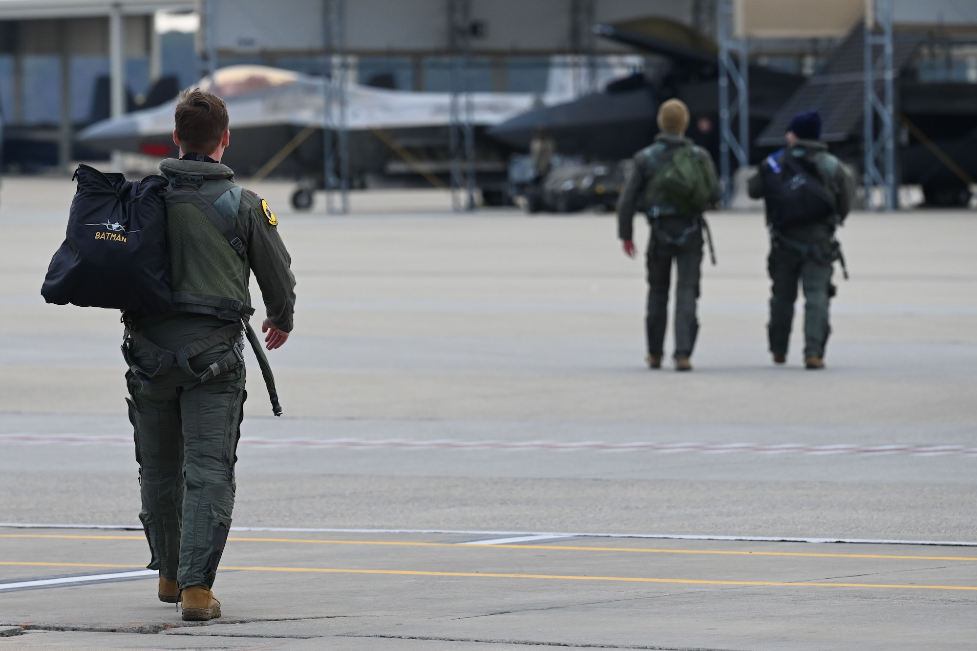 A pilot carrying a bag on the flightline walks towards F-22s